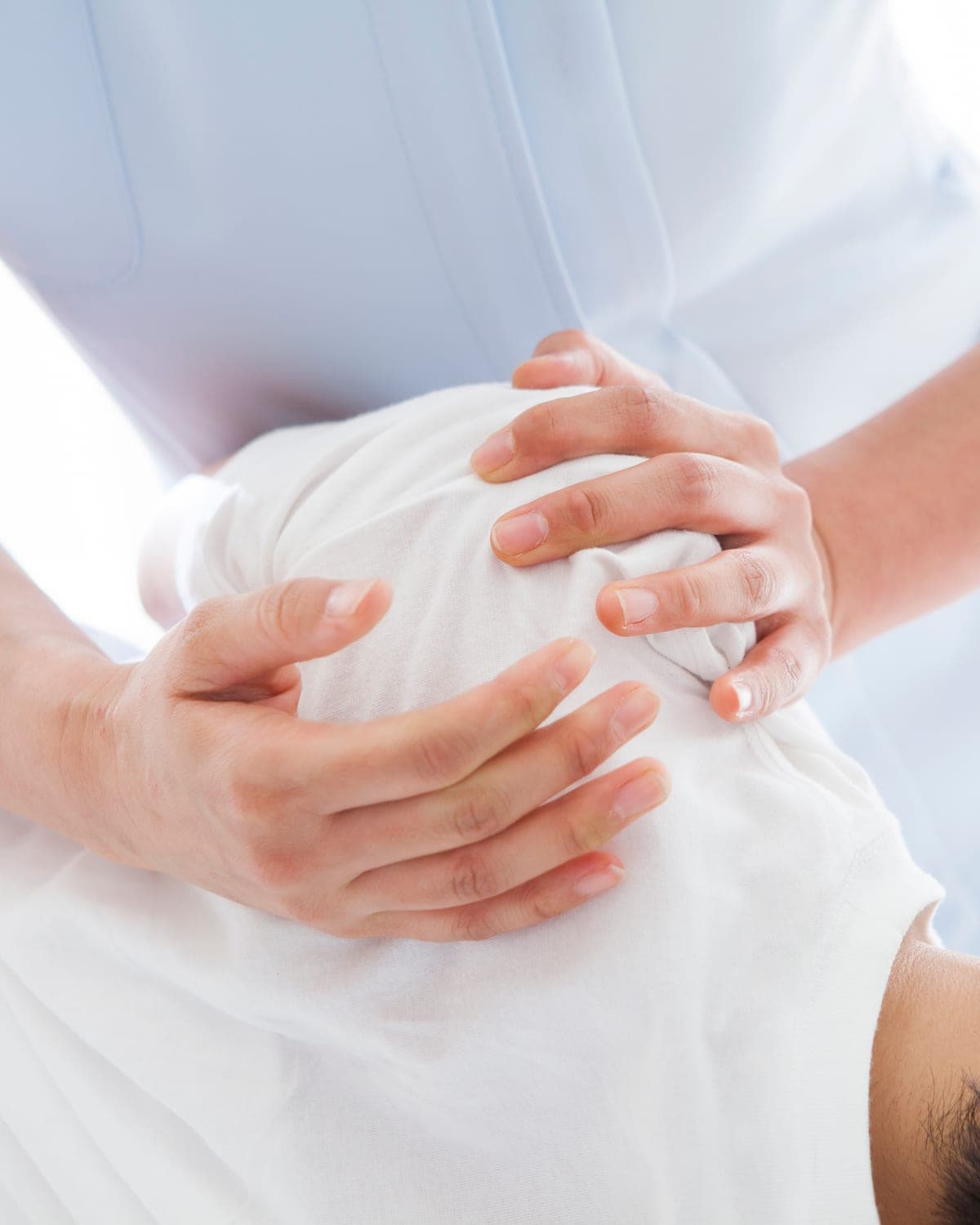 Séance d’ostéopathie, mains du praticien sur l’épaule d’un patient